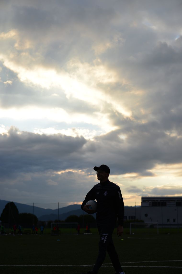 Predrag Bibu mit einem Ball unter dem Arm auf dem Trainingsplatz, im Gegenlicht vor Abendwolken